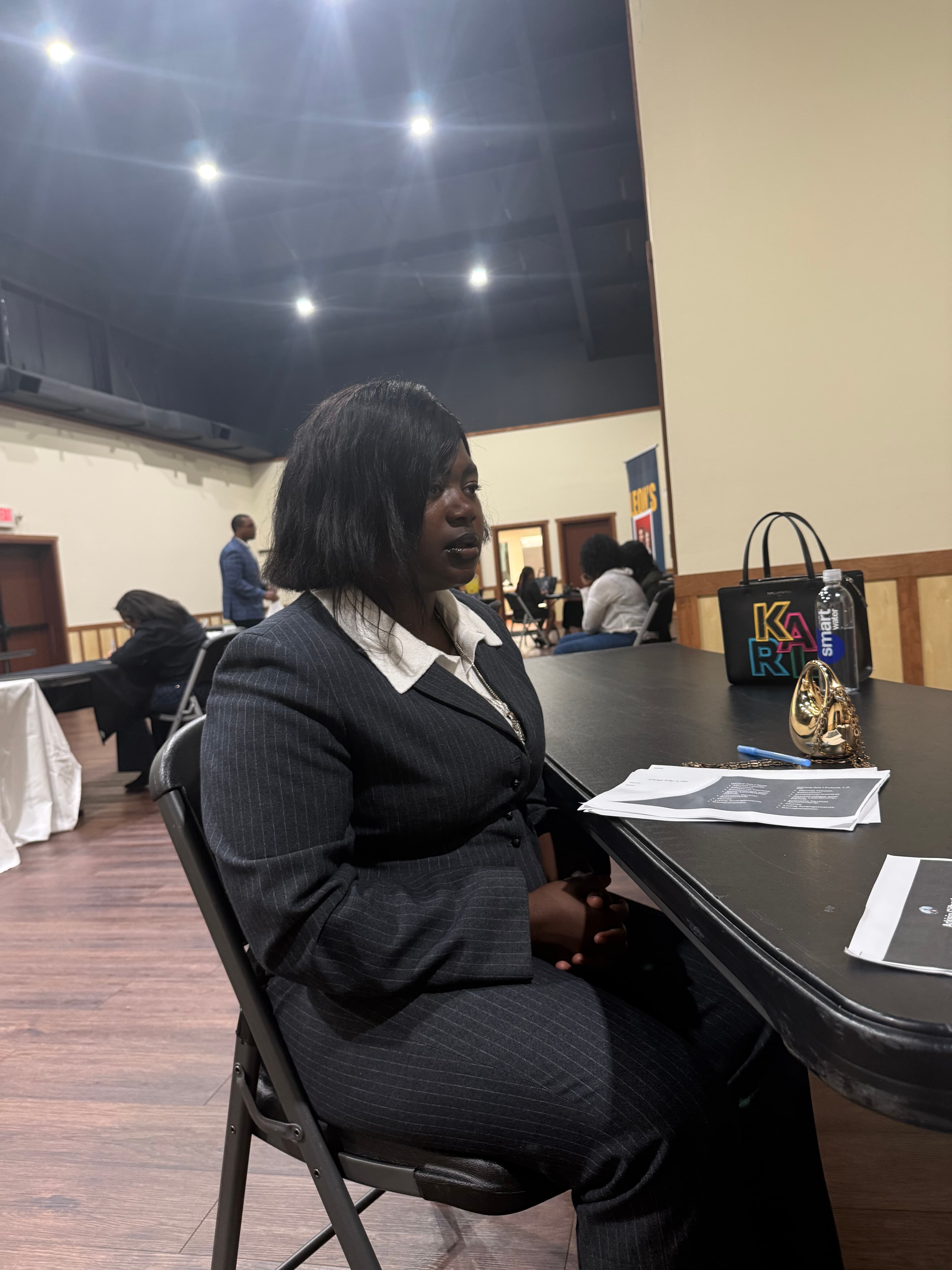 Woman in a pinstripe suit sits at a table with papers and accessories.