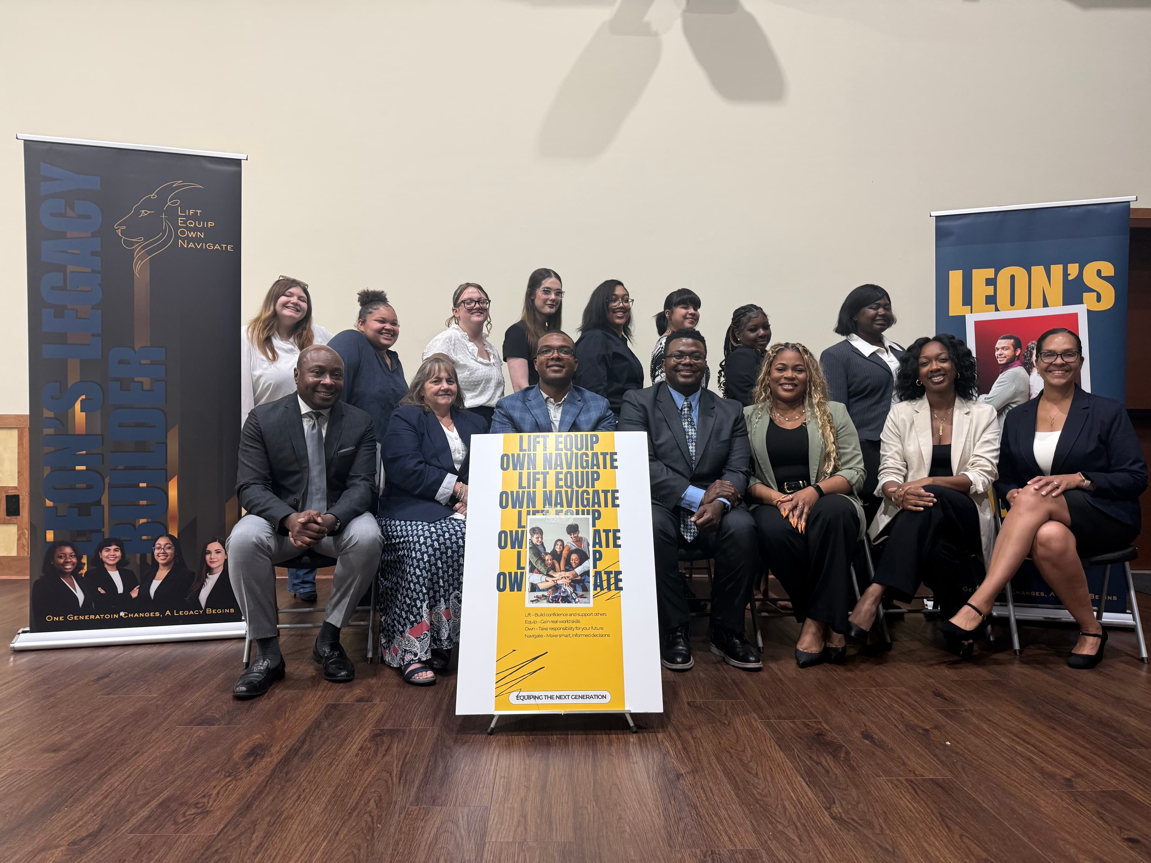 Diverse group of people posing for a photo with "LIFT EQUIP OWN NAVIGATE" signage.