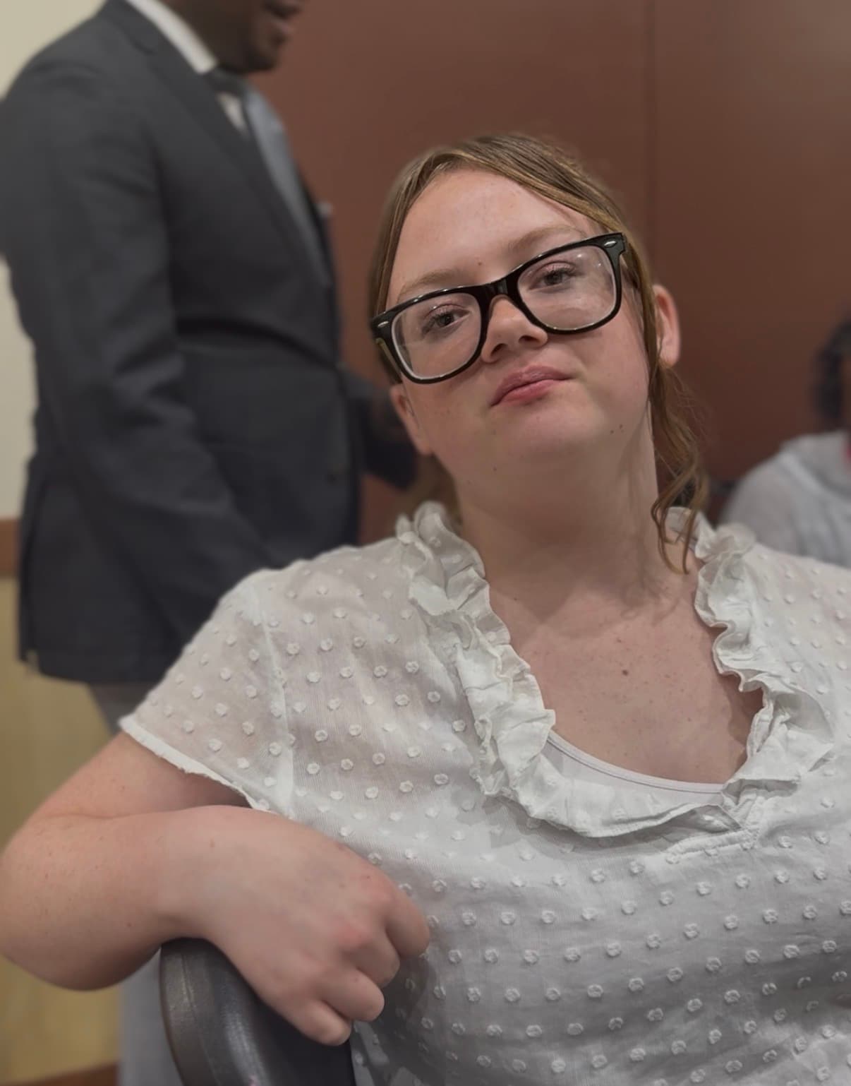 Young woman with black-rimmed glasses and a white ruffled blouse looking directly at the camera.