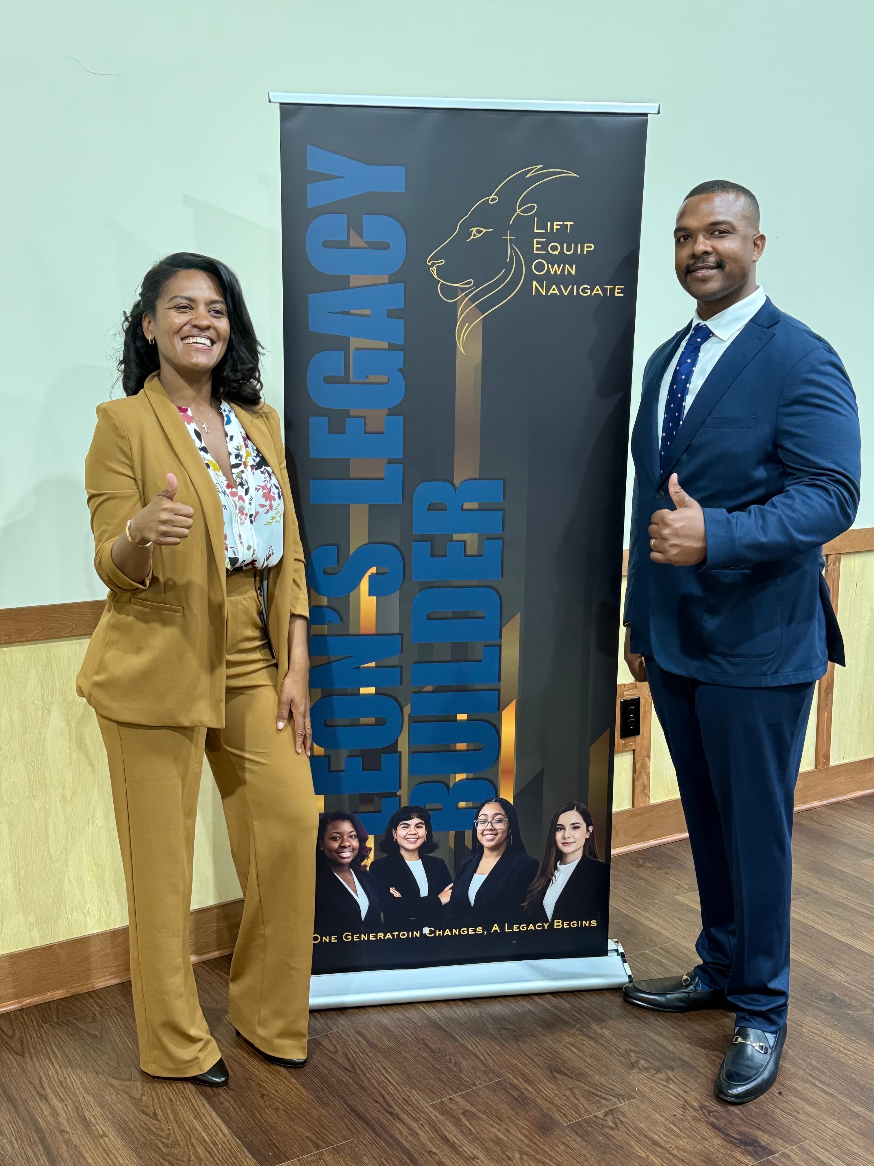 Smiling man and woman in suits giving thumbs up beside a Leon's Legacy Builder banner.